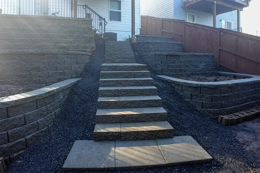Backyard hardscape construction with retaining walls, stone stairs, gravel paths, and tiered landscaping in Newberg, Oregon